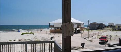 A beach view with a wooden deck, a white tent, and a red car parked on the sand.
