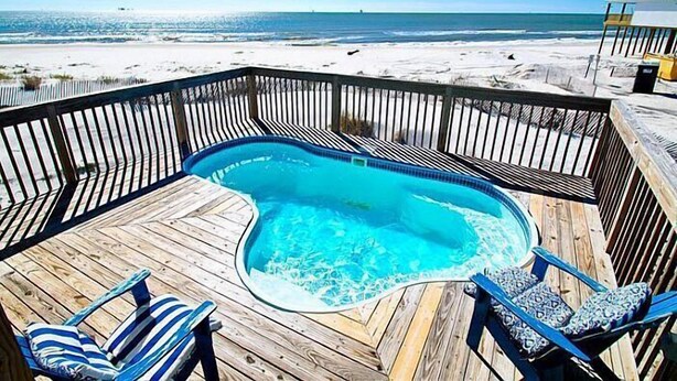Une terrasse en bois avec un jacuzzi, deux chaises à rayures et une vue sur la plage et l’océan.