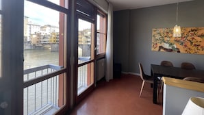 Une pièce dotée de grandes fenêtres donnant sur une rivière, un coin repas avec des chaises et une table, et un tableau accroché au mur.