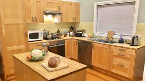 A kitchen with wooden cabinets, a microwave, a stove, and a sink. - Grevillea Cottage - Family and Group Getaways (Katoomba)