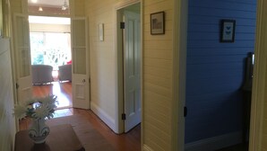 A hallway with wooden floors, a door leading to a room with blue walls, and a vase with flowers on a table. - Grevillea Cottage - Family and Group Getaways (Katoomba)
