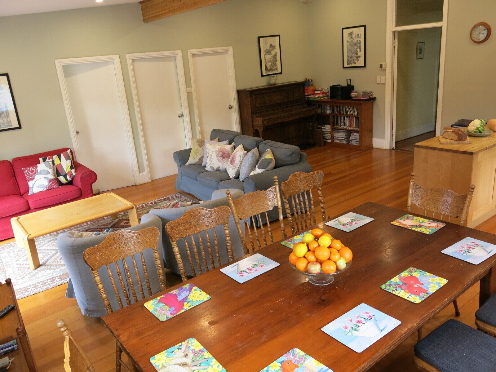 Un comedor con una mesa de madera dispuesta para seis personas, rodeada por seis sillas. Hay un frutero sobre la mesa.