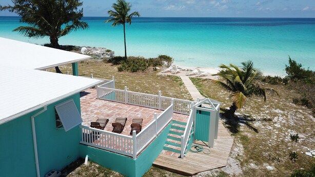 A turquoise building with a patio area, a wooden deck, and a view of the ocean. - The nicest beach house in Great Harbour,   Guaranteed!   Enjoy🏝 (Great Harbour Cay, Bahamas (GHC))