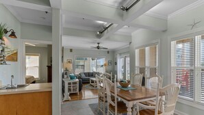 A spacious kitchen with a wooden island, a dining area with white chairs, and a view of the living room. - CottageVacations4u "MEANT 2B" -pool club- ocean view-200 FT to beach. DOG FRIENDLY. (Ocean Isle Beach)