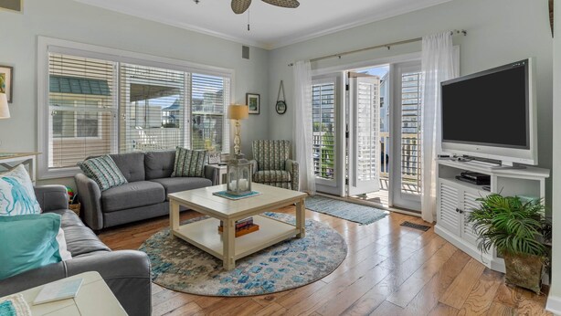 A spacious living room with a grey sofa, a coffee table, a TV, and a ceiling fan. - CottageVacations4u "MEANT 2B" -pool club- ocean view-200 FT to beach. DOG FRIENDLY. (Ocean Isle Beach)