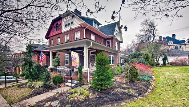 Ein zweistöckiges Haus mit Veranda, Backsteinfassade und einem kleinen Garten mit verschiedenen Pflanzen und Rasenfläche.