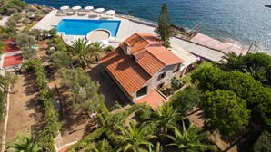 Vista aérea de una propiedad con piscina, edificio de tejas rojas y vistas al mar.
