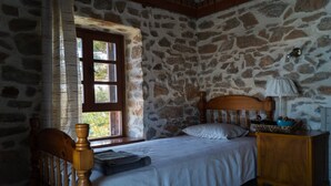 Un dormitorio con pared de piedra, cama de madera con cabecera, mesita de noche y ventana con cortinas.