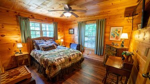 A wooden cabin bedroom with a bed, a desk, a chair, a dresser, and a ceiling fan. - Haven in the Hills! Spectacular Views, River Access, & 5-Star Amenities! (Murphy)