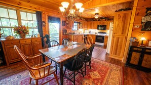 A wooden cabin interior with a dining area, kitchen, and a large window. - Haven in the Hills! Spectacular Views, River Access, & 5-Star Amenities! (Murphy)