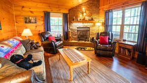 A cozy log cabin interior with a fireplace, leather furniture, and large windows. - Haven in the Hills! Spectacular Views, River Access, & 5-Star Amenities! (Murphy)