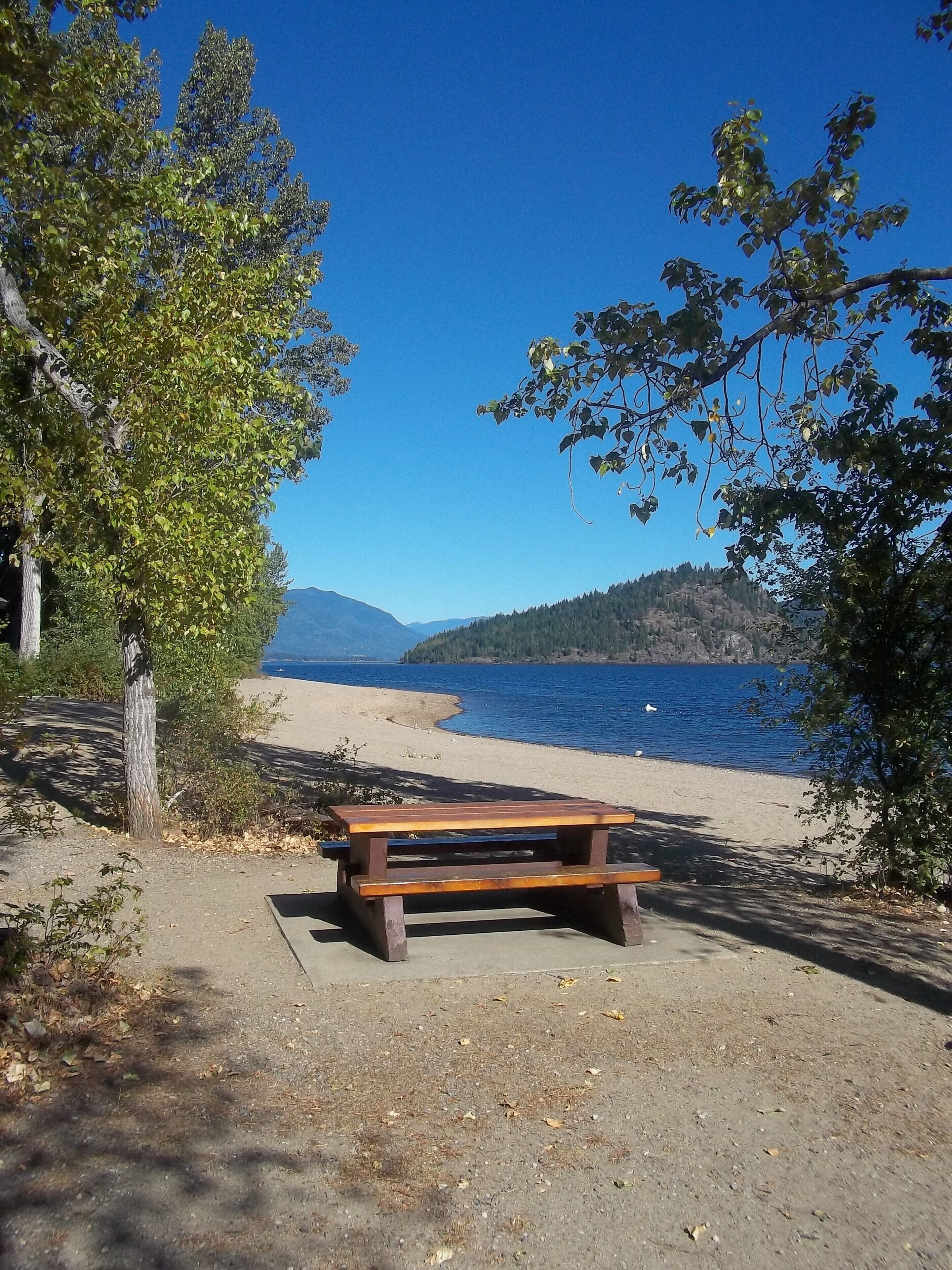 A picnic table by a lakeside with a clear view of the water and distant mountains.