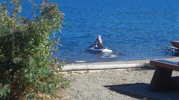 A lakeside view with a person on a jet ski, a picnic table, and a grassy area.