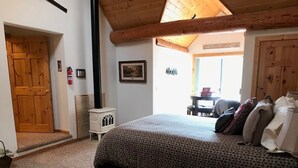 Une chambre à coucher avec un grand lit, un plafond en bois, une cheminée et une porte donnant sur une autre pièce.