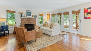 A spacious living room with hardwood floors, a fireplace, a white sofa, and large windows.