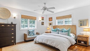 A bedroom with a bed, a dresser, a nightstand, a ceiling fan, and a window with a view of trees.
