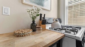 A kitchen with a gas stove, a kettle, a vase with flowers, and a cork coaster set. - 1890s Gem | Prime Midtown Hub | Walk to Everything (Sacramento)