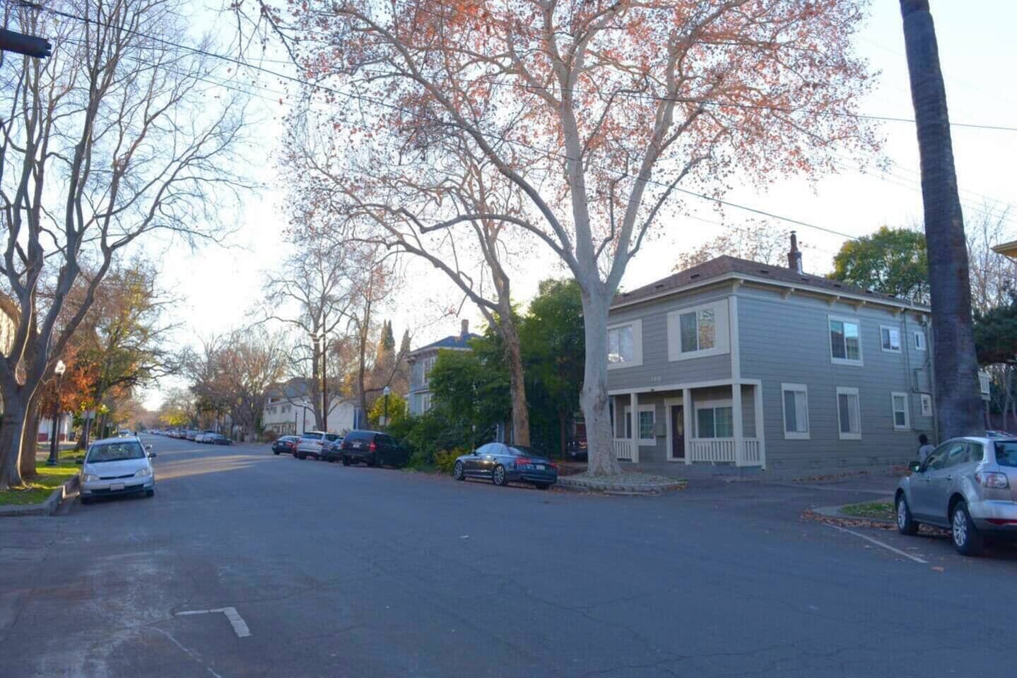 A residential street with two-story houses, parked cars, and leafless trees.