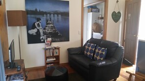 Un salon avec un canapé en cuir noir, une bibliothèque remplie de livres, un tableau accroché au mur et un objet décoratif en forme de cœur.