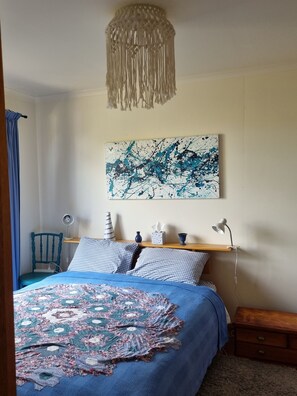 Een slaapkamer met een bed, een hanglamp, een wanddecoratie in abstractie, een stoel en nachtkastjes.