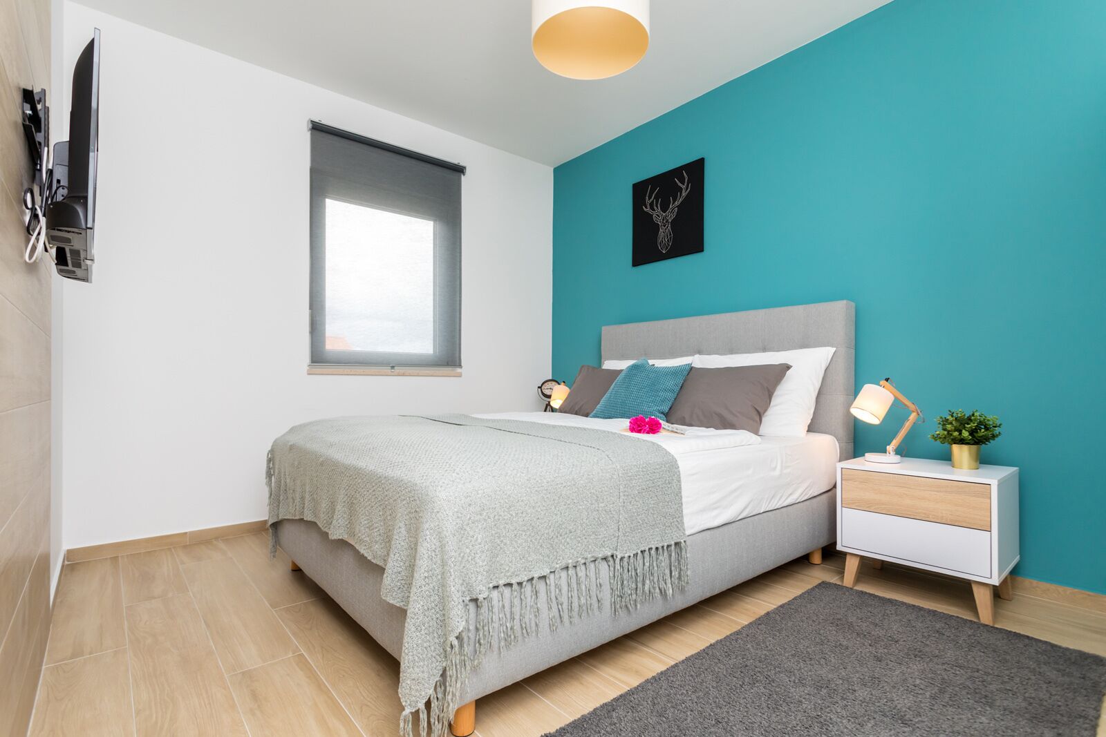 A modern bedroom with a bed, bedside table, lamp, and a wall-mounted artwork.