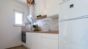 A modern kitchen with white cabinets, a built-in oven, a stainless steel sink, and a white refrigerator.