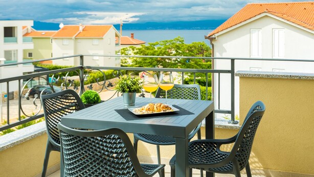 A balcony with a table set for two, a potted plant, and a glass of orange juice.