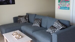 A living room with a grey sofa, patterned cushions, a white coffee table, and a 'Welcome' sign with flamingos. - Waterfront condo with private balcony. Sun All Day! (St. Petersburg)