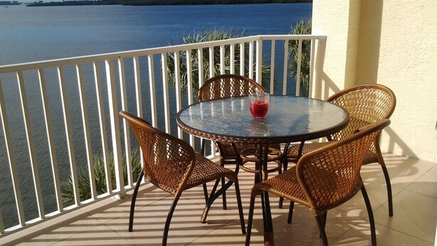 A round table with wicker chairs on a balcony overlooking a body of water. - Waterfront condo with private balcony. Sun All Day! (St. Petersburg)