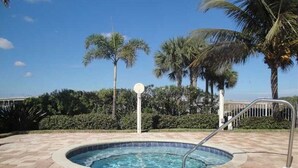A swimming pool with a tiled deck, surrounded by palm trees and a clear sky. - Waterfront condo with private balcony. Sun All Day! (St. Petersburg)
