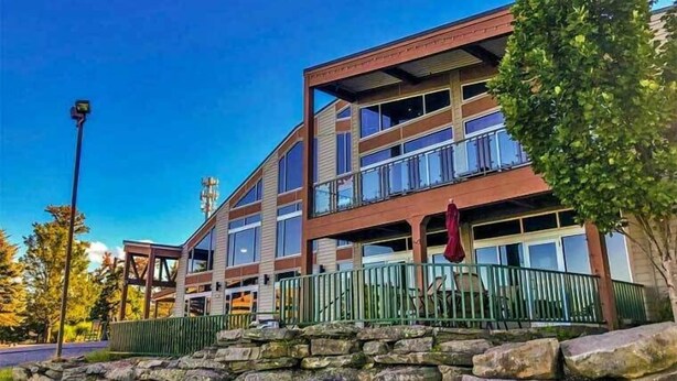 A multi-story building with a stone foundation, large windows, and a green metal fence. - Ski-In/Out, 2 Game Theaters, Hibachi Grill, 2 Masters, Hot Tub & Slope Views (Lackawaxen)