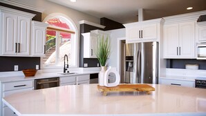 A modern kitchen with white cabinetry, a stainless steel refrigerator, and a large island. - Executive Getaway close to all the action with Private 2 slip dock  (Sunrise Beach)