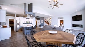 Una cocina moderna con armarios blancos, una isla central y un comedor con mesa y sillas de madera.
