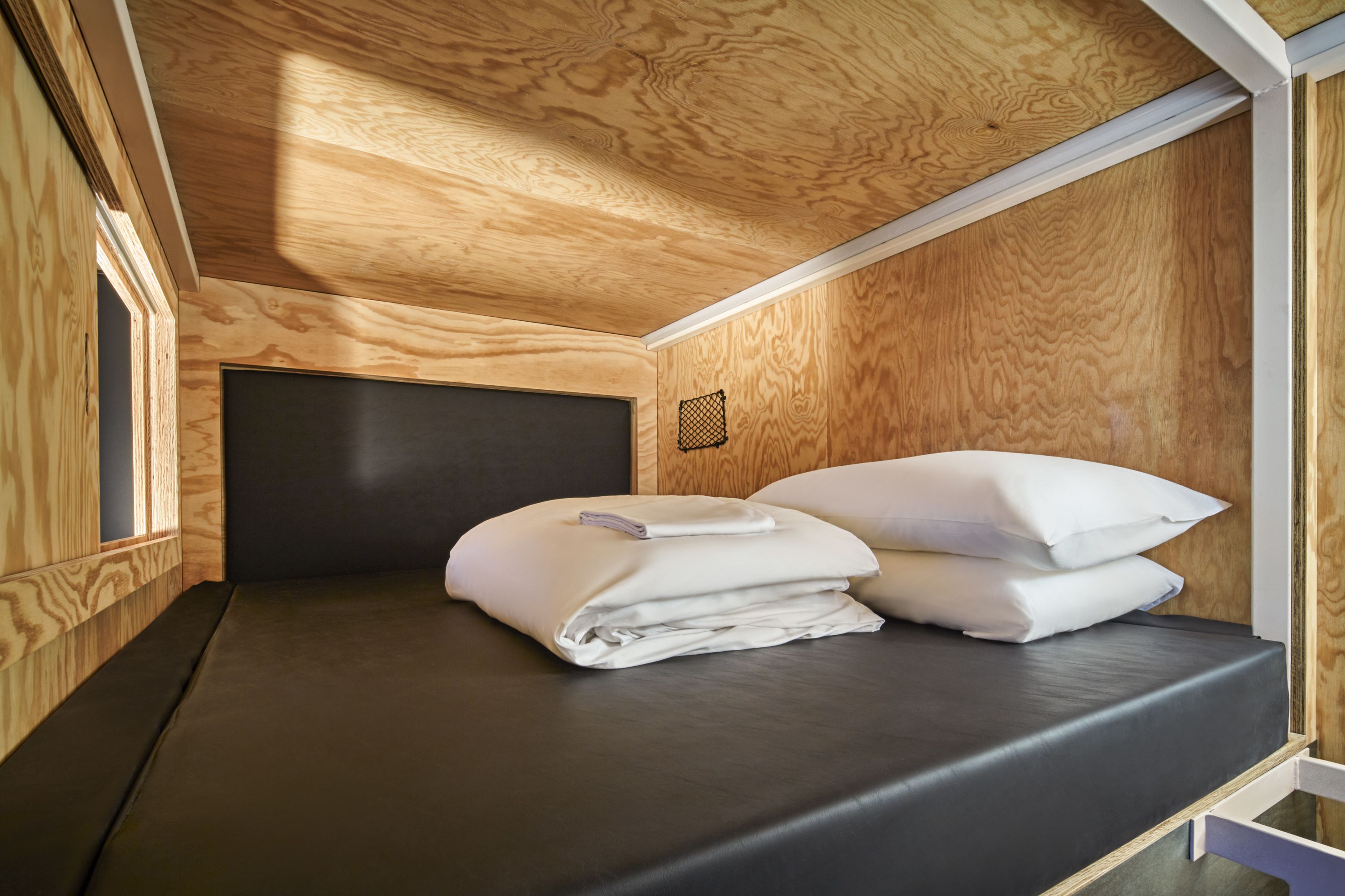 A compact room with a bed, wooden walls, and a slanted ceiling.