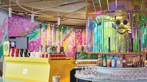 A bar area with a colorful mural, a yellow counter, and a variety of bottles and glasses. - JO&JOE Paris - Gentilly Hotel - Hostel (Gentilly)