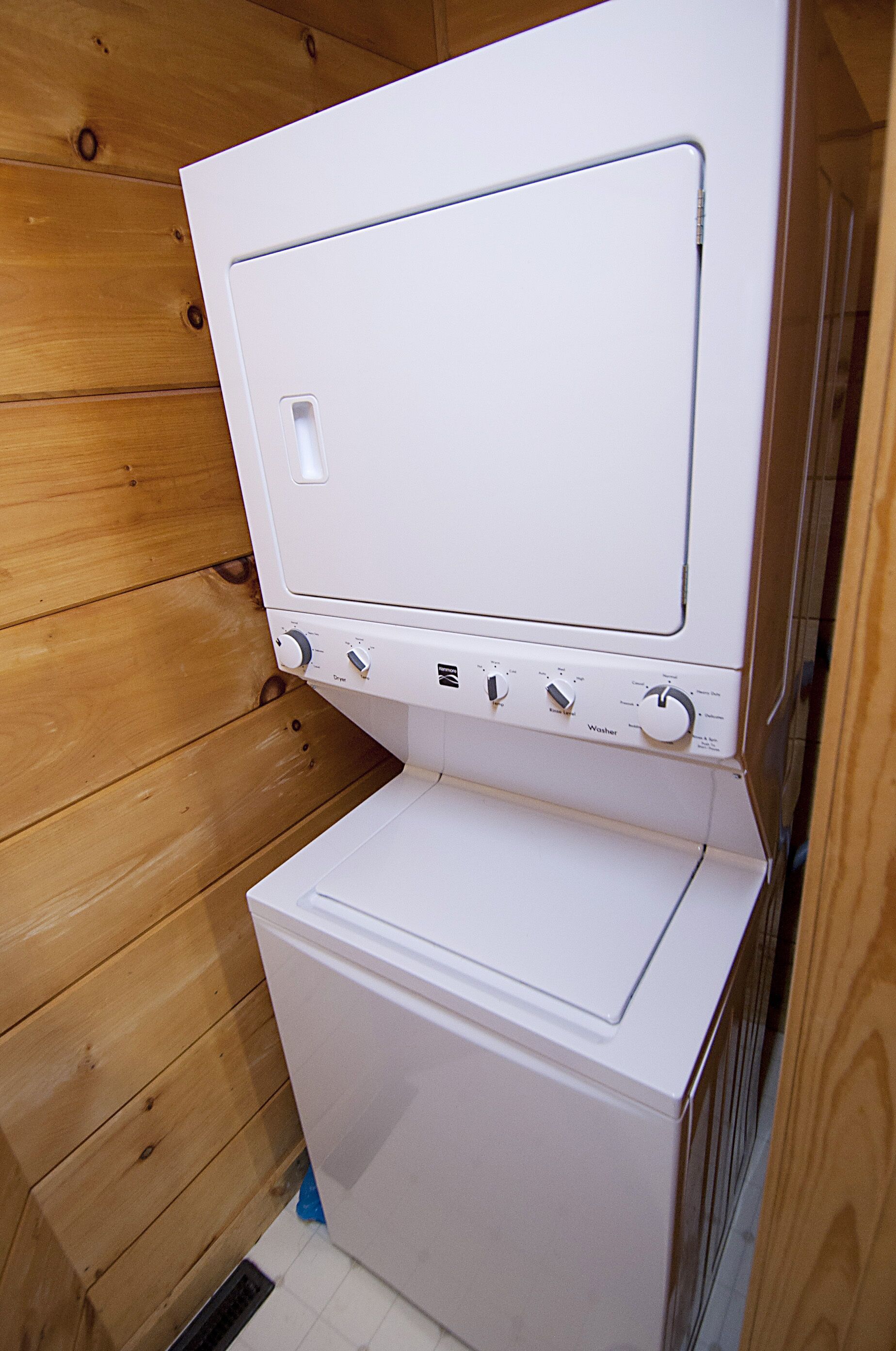 Lavadora y secadora compactas, blancas y de dos puertas, con perillas de control y una pequeña pantalla, instaladas en una habitación con paneles de madera.