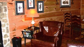 A cozy room with a leather armchair, a small table with a lamp, and framed pictures on the wall. - Clean, Secluded yet Convenient to Town, Well Stocked Cabin in the Woods! Wi-fi! (Townsend)