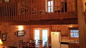 A cabin interior with a dining area, kitchen, and a loft bedroom with a balcony. - Clean, Secluded yet Convenient to Town, Well Stocked Cabin in the Woods! Wi-fi! (Townsend)