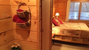 A wooden cabin room with a bed, a small window, and a bathroom with a bathtub. - Clean, Secluded yet Convenient to Town, Well Stocked Cabin in the Woods! Wi-fi! (Townsend)