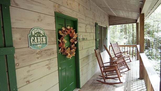 A cabin with a green door, a welcome sign, and a porch with wooden rocking chairs. - Clean, Secluded yet Convenient to Town, Well Stocked Cabin in the Woods! Wi-fi! (Townsend)