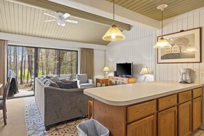 Una sala de estar moderna con un sofá, televisor y una zona de cocina con cafetera.