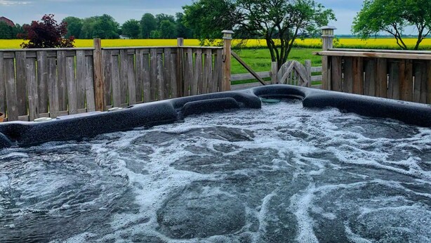 A hot tub with a wooden fence and trees in the background.