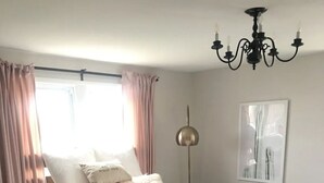 A bedroom with a large bed, wooden platform, fluffy rug, curtains, a chandelier, and a wall-mounted artwork.