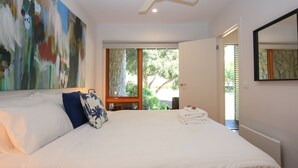 Une chambre avec un grand lit, un tableau au mur et une vue sur la verdure à l’extérieur.