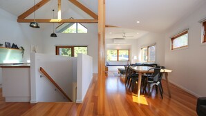 Une cuisine moderne avec des poutres en bois, un coin repas avec une table et des chaises en bois, et de grandes fenêtres qui laissent entrer la lumière naturelle.