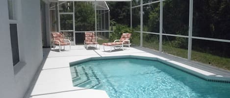 Piscina com estrutura de vidro, cercada por paredes brancas e algumas cadeiras de descanso.