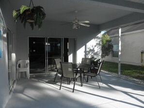 A covered patio area with a table and chairs, a ceiling fan, and a sliding glass door leading to a covered outdoor space. - Relaxing Vacation Home w/ Lake,Golf,Pool,Tennis,Internet,Cable,Sunsets (Davenport)