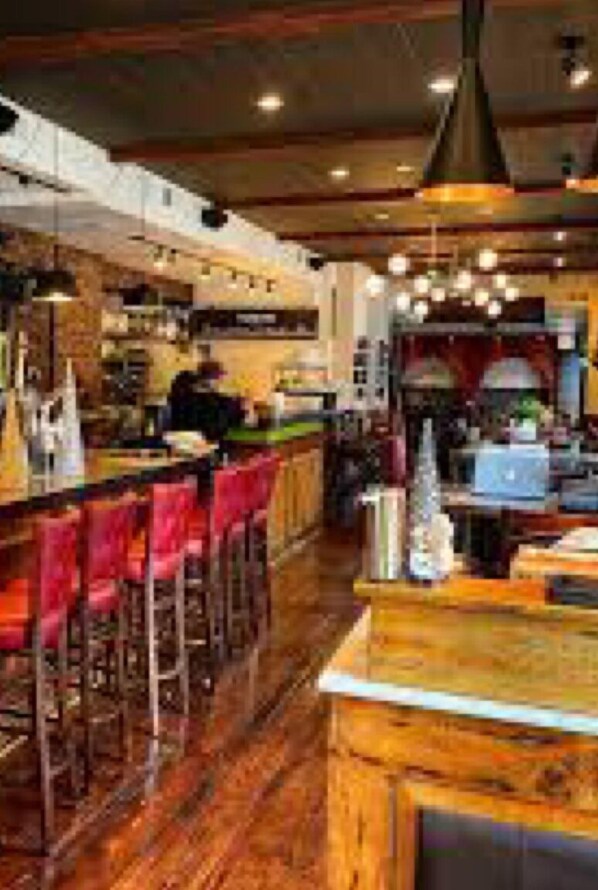 A restaurant interior with wooden flooring, red bar stools, and a bar counter.