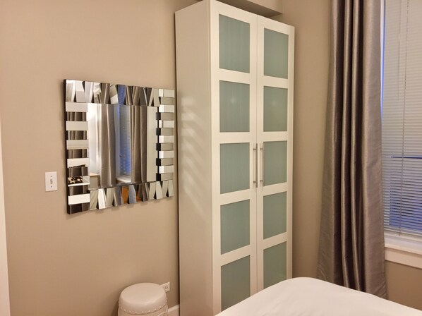 A bedroom with a bed, a wardrobe, a mirror, and a window with curtains.