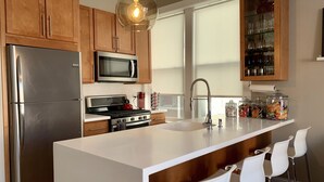 Una cocina moderna con armarios de madera, electrodomésticos de acero inoxidable, una isla blanca con taburetes y un mueble de vidrio con cristalería.
